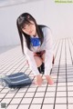 A young woman in a school uniform crouching on the ground.