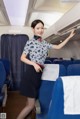 A woman in a blue and white uniform standing in an airplane.