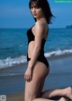 A woman in a black bathing suit sitting on the beach.