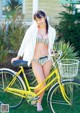 A woman in a bikini standing next to a yellow bike.