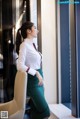 A woman in a white shirt and green skirt leaning against a wall.