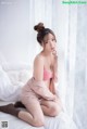 A woman in a pink lingerie sitting on a bed.