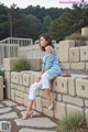 A woman sitting on a stone wall wearing white pants and a blue sweater.